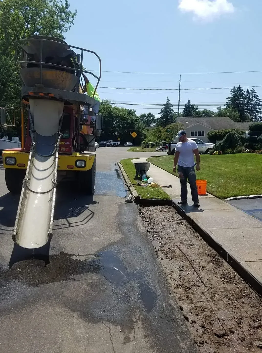 Crew members stage a curb trench with rebar as a cement mixer prepares to pour concrete.