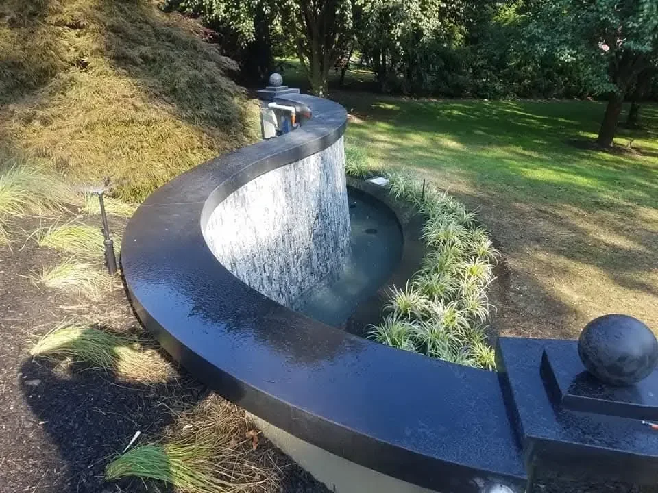 A curved black stone wall spills water into a landscaped garden basin.