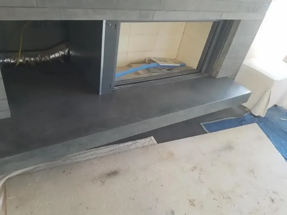 This image captures an unfinished fireplace installation featuring a dark hearth, gray stone surround, and exposed flexible ductwork and wiring within the firebox opening.