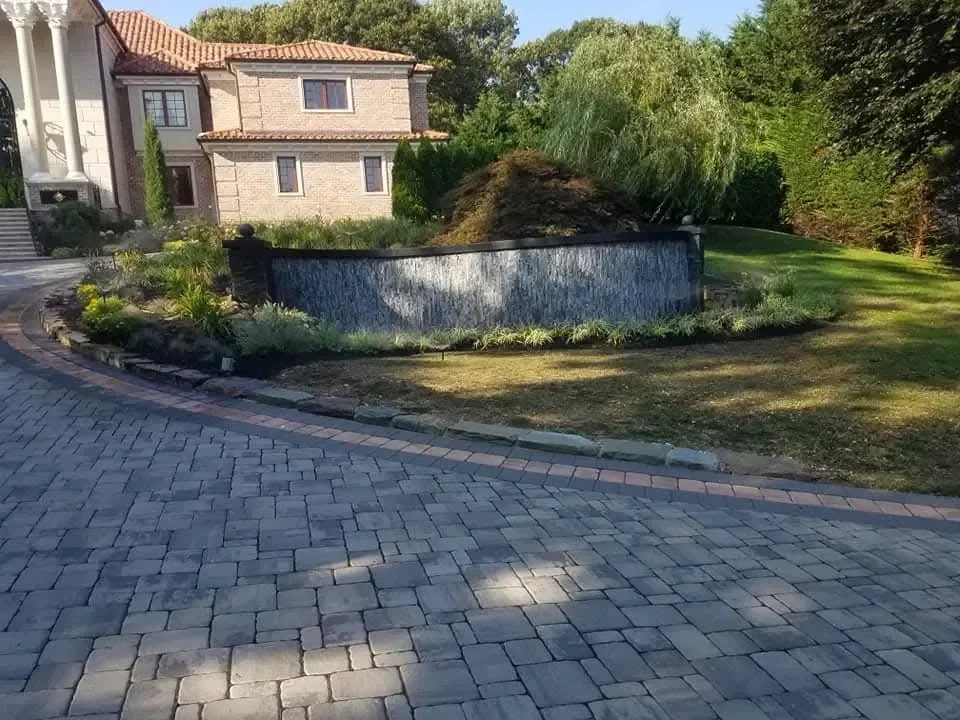 A curved stone water wall and paver driveway welcoming guests to a luxury brick home.