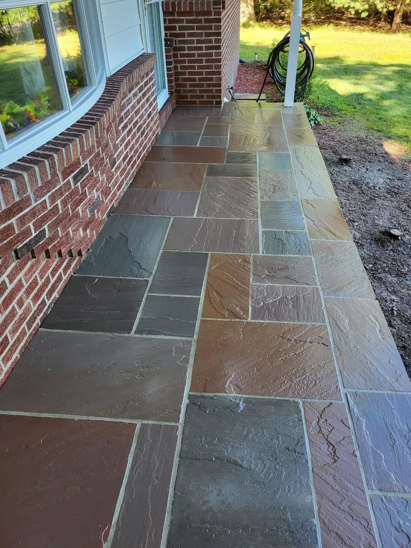 A textured flagstone walkway runs alongside a red brick exterior wall.