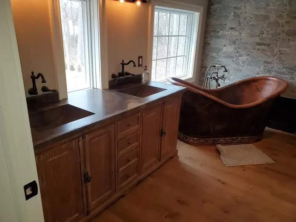 This luxurious rustic bathroom features a large copper freestanding tub, a double wooden vanity, and a striking natural stone accent wall.