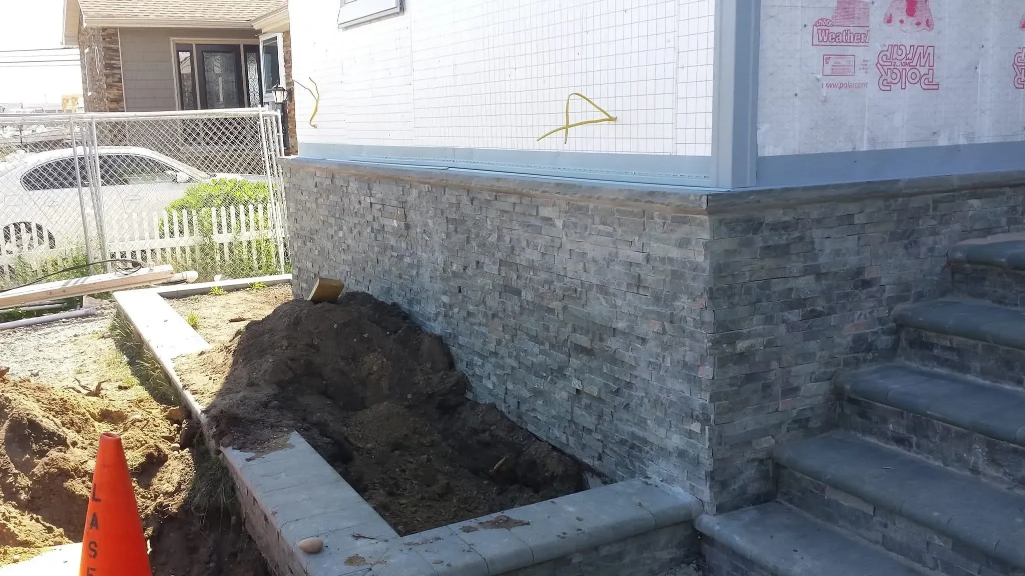 Dark stacked stone veneer is added to a home's foundation while siding awaits finishing.