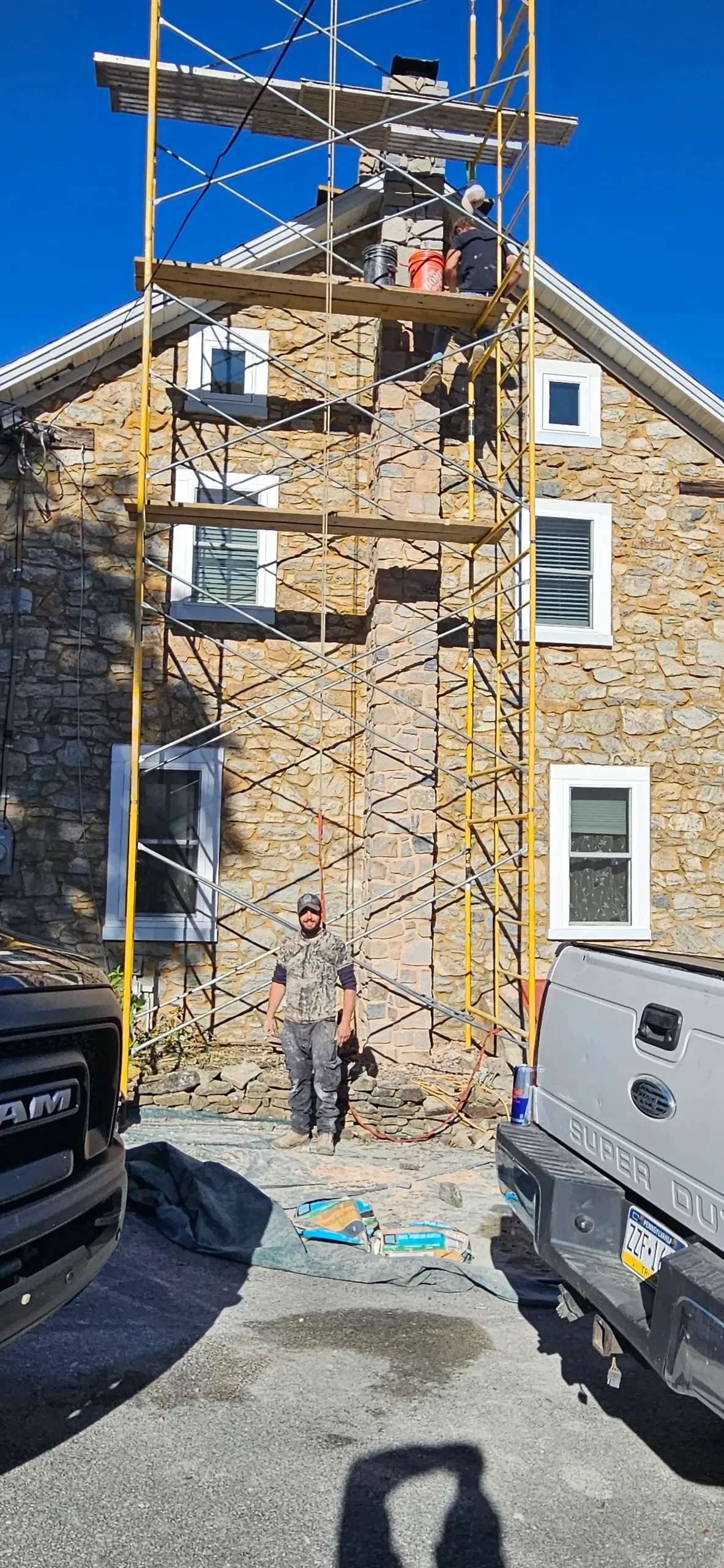 Two masons stand on tall scaffolding to restore a stone chimney façade.