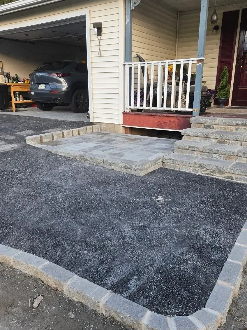 New stone edging borders a gravel strip beside a gray paver landing and natural stone steps.